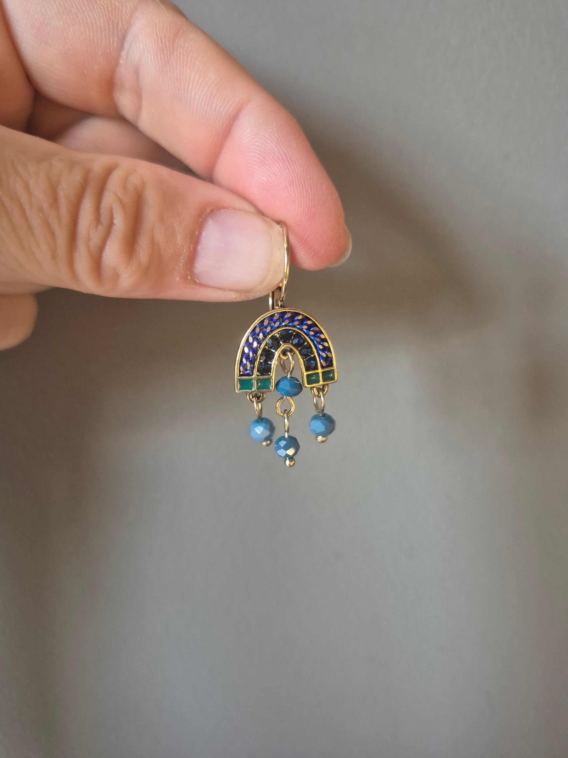 Hand holding a decorative earring with blue stones against a neutral background