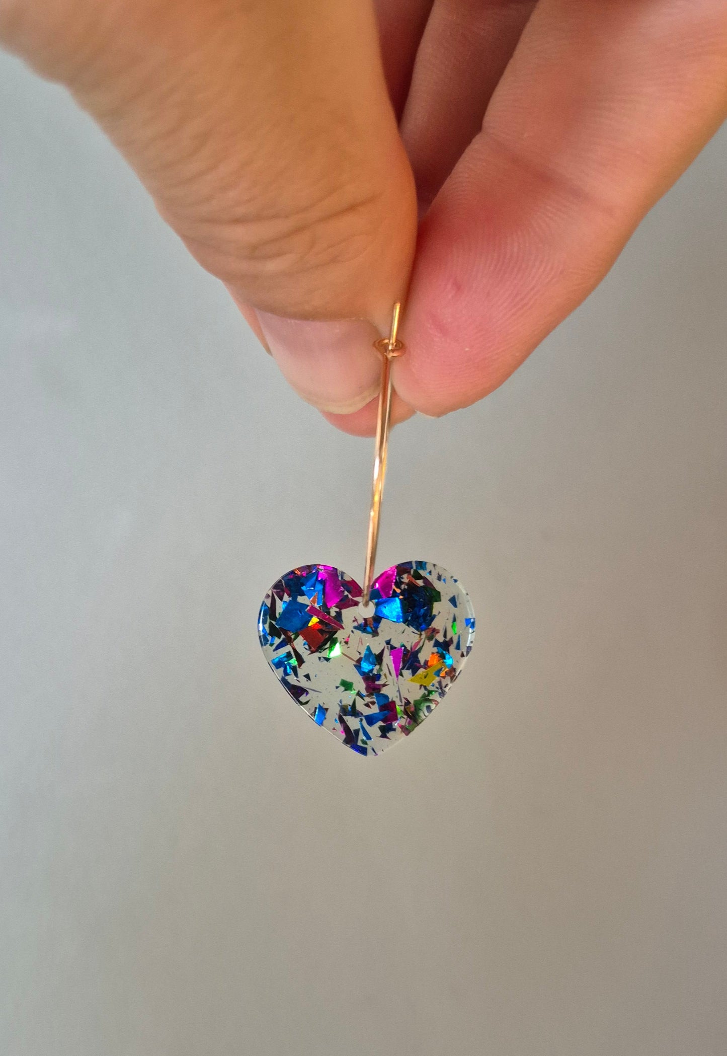 Hand holding a decorative brooch with multicolored gemstones against a plain background