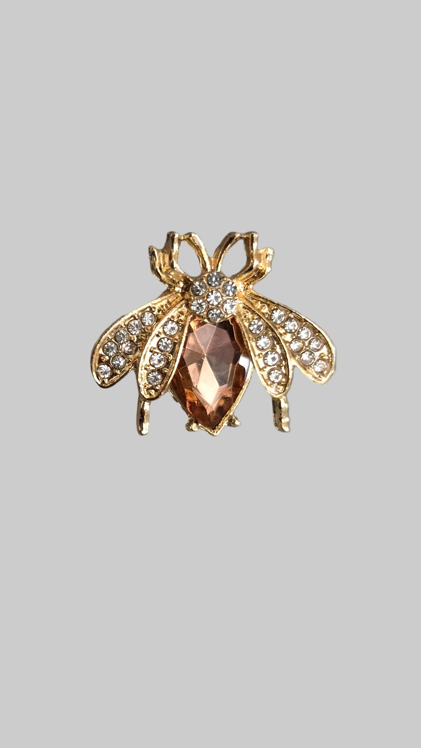 Gold bee-shaped brooch with a central gemstone on a gray background
