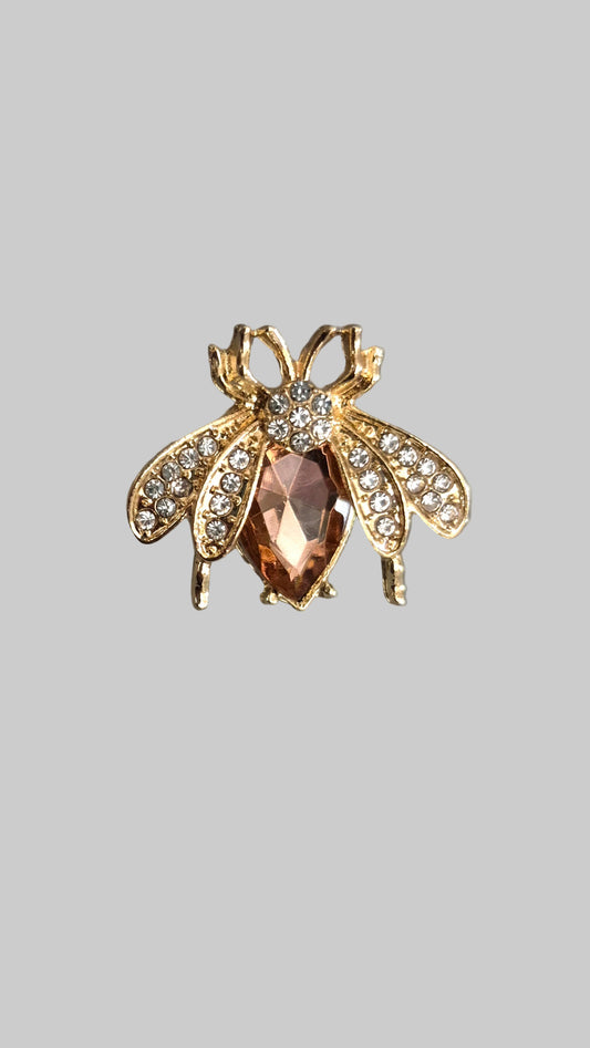 Gold bee-shaped brooch with a central gemstone on a gray background