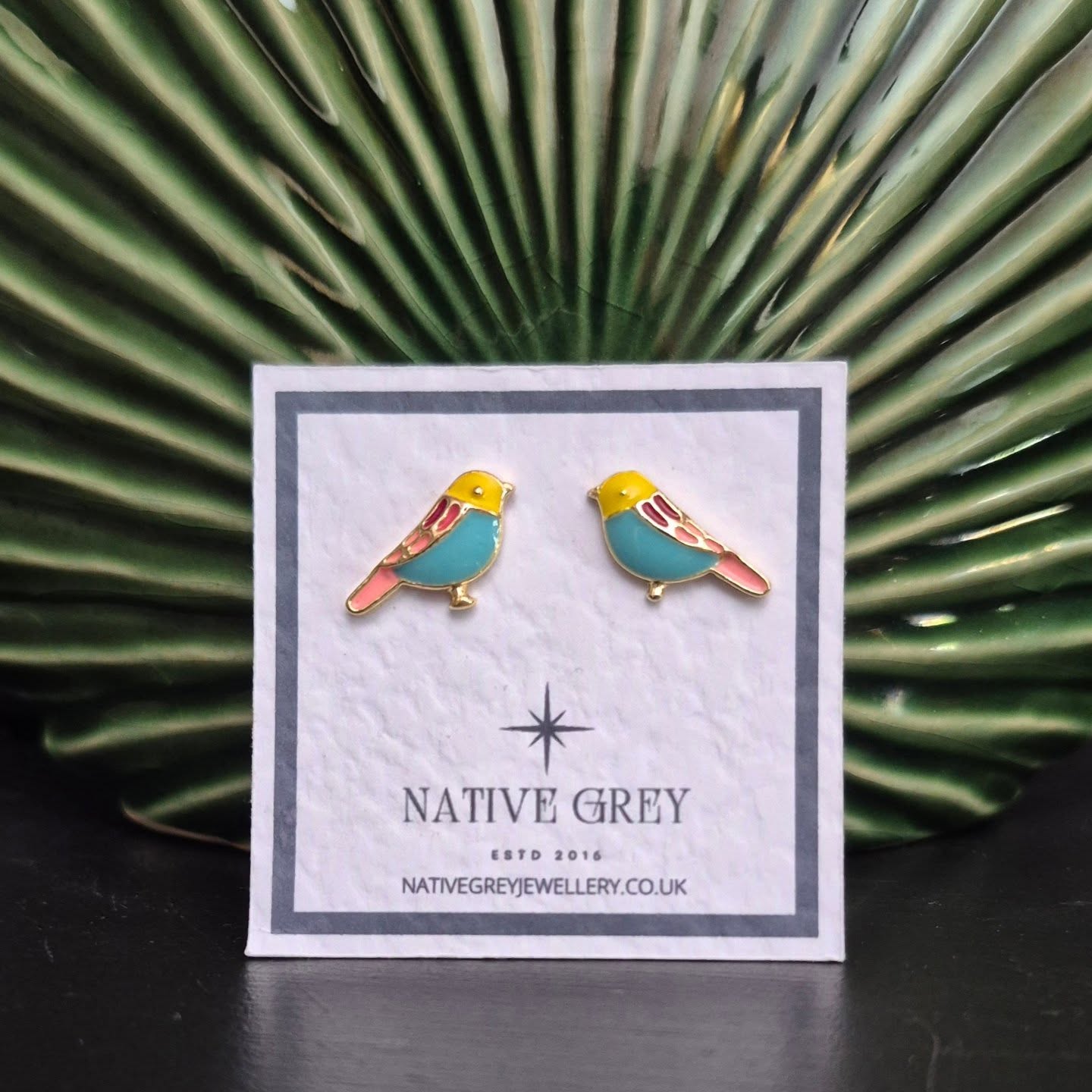 Bird-shaped earrings on a Native Grey branded card with a green leafy background