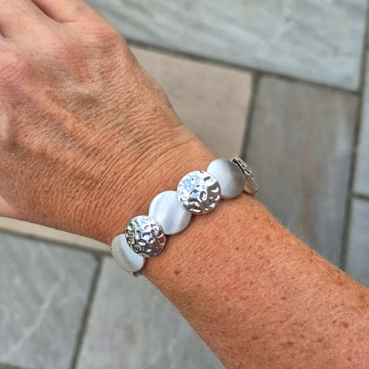 White bracelet with silver beads on a wrist against a tiled wall background
