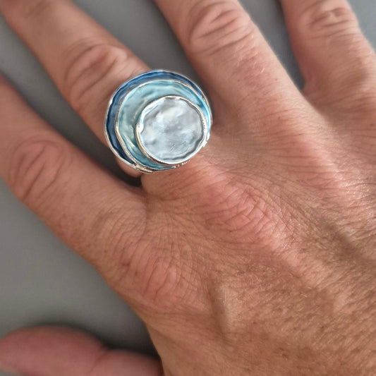 Hand wearing a silver ring with a blue stone on a gray background