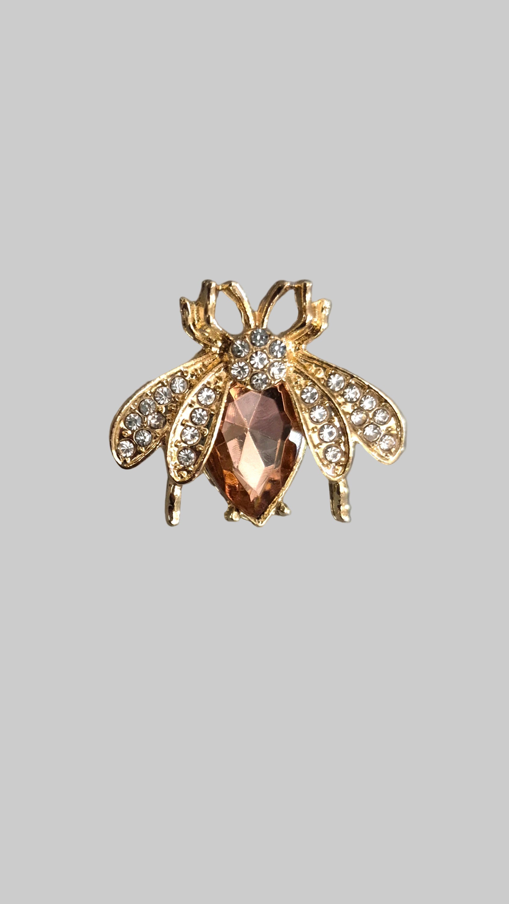 Gold bee-shaped brooch with a central gemstone on a gray background