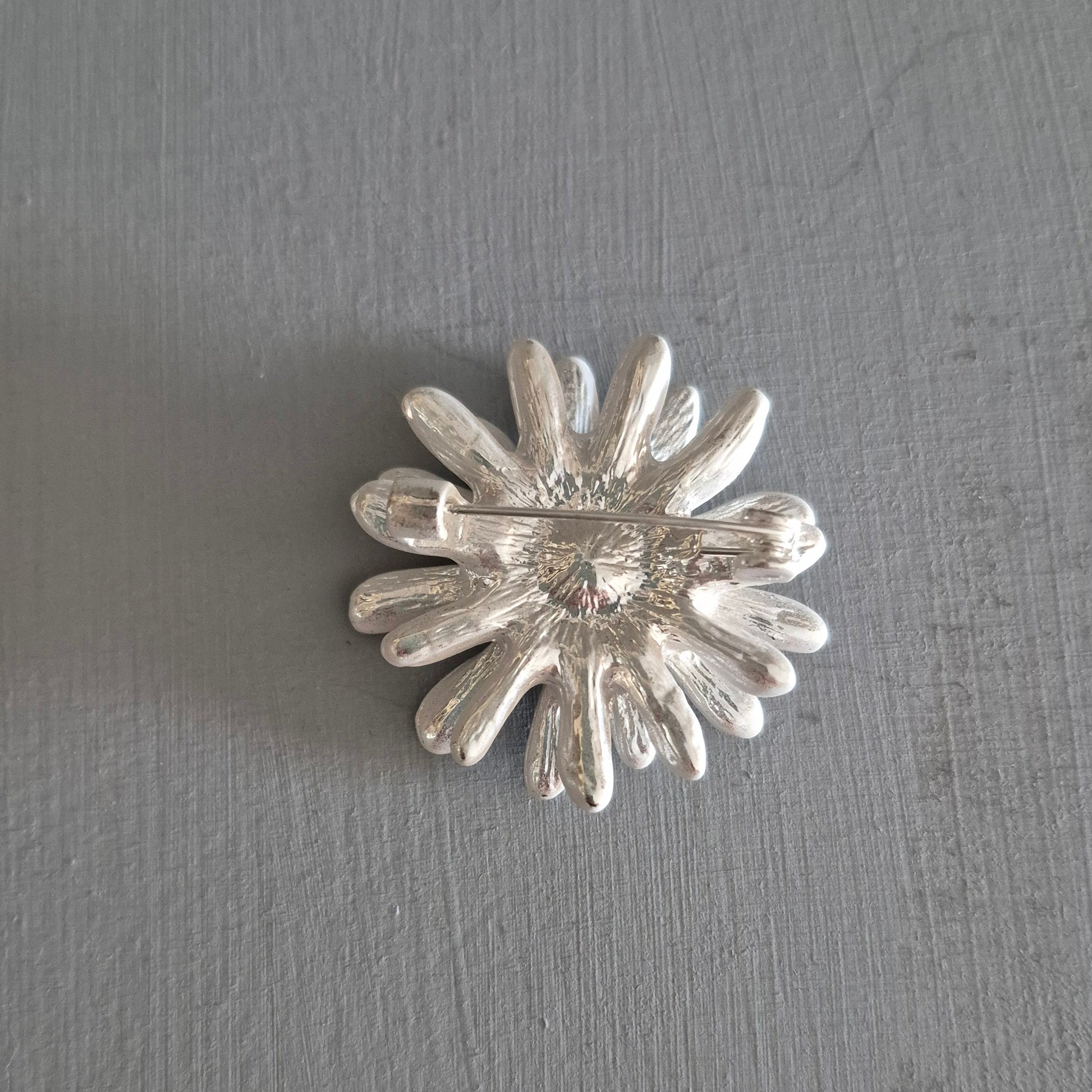 Silver flower-shaped brooch on a gray background
