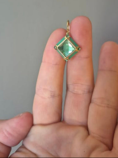 Gold pendant with a green gemstone held between fingers against a neutral background